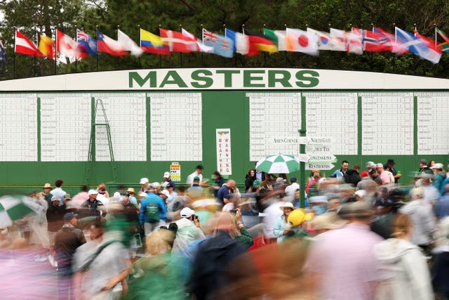 Crowd at a golf tournament under flags with a scoreboard in the background.