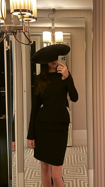 woman in a black outfit and large hat in a mirrored setting