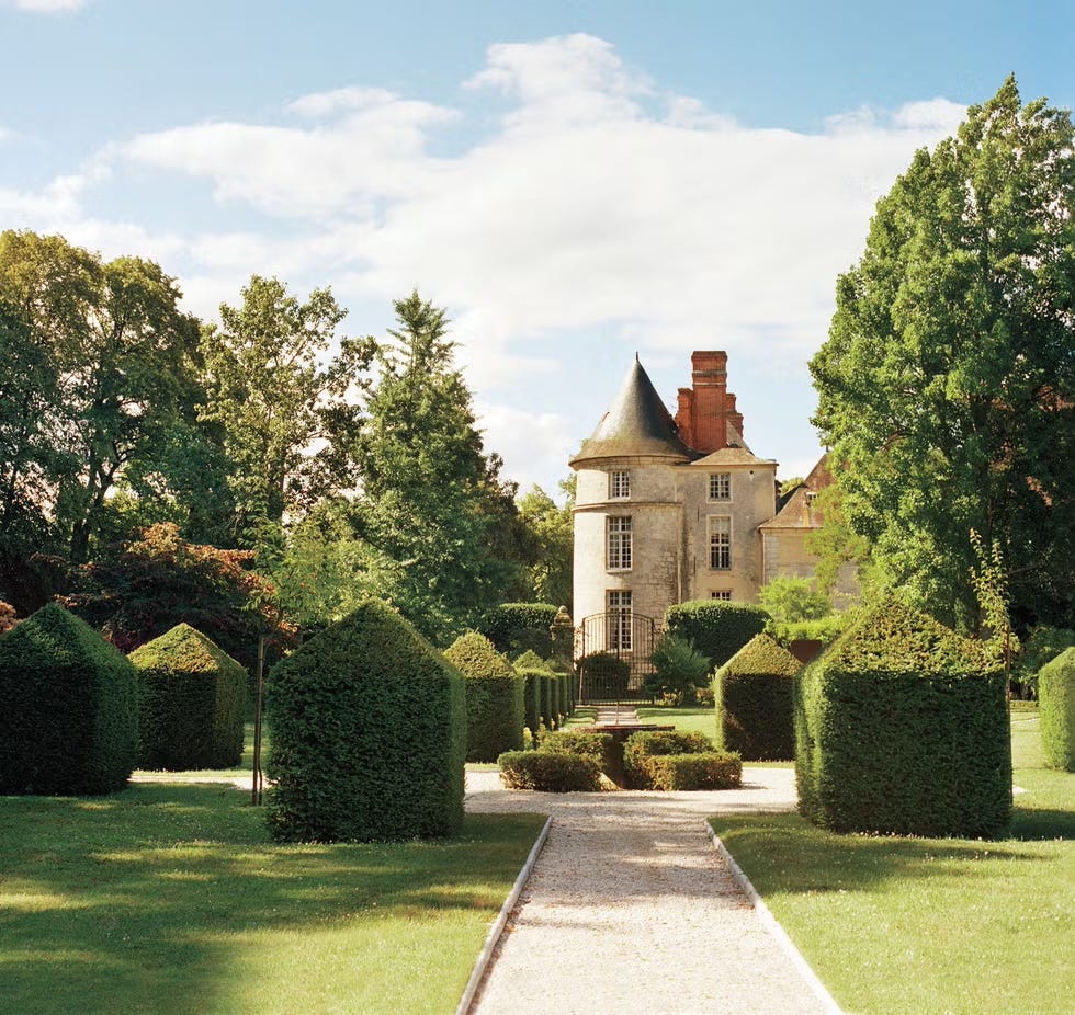 A landscaped garden featuring manicured hedges and a stone house.