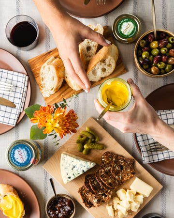 a spread of food items including bread cheese olives and ghee with hands preparing to serve