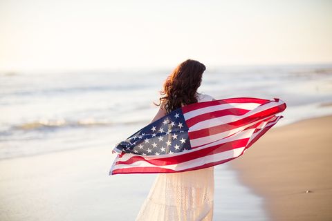 4th of july activities woman wearing white dress walking on a beach with american flag