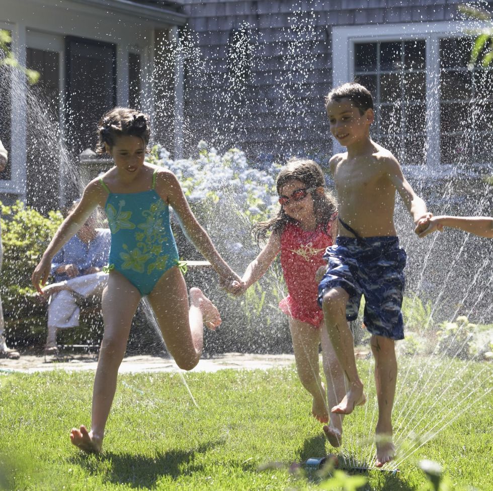 group of four children playing around a sprinkler in a garden on 4th of july