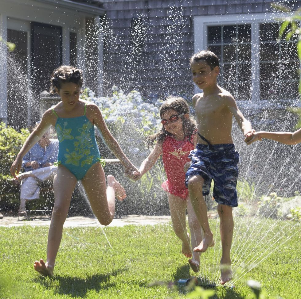 group of four children playing around a sprinkler in a garden on 4th of july