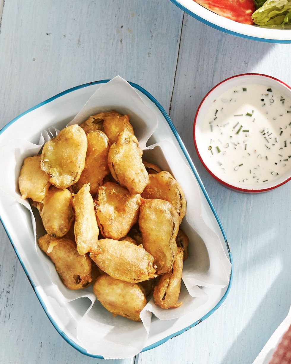 fried pickles in a parchment lined serving tray with a bowl of buttermilk ranch to the side for dipping