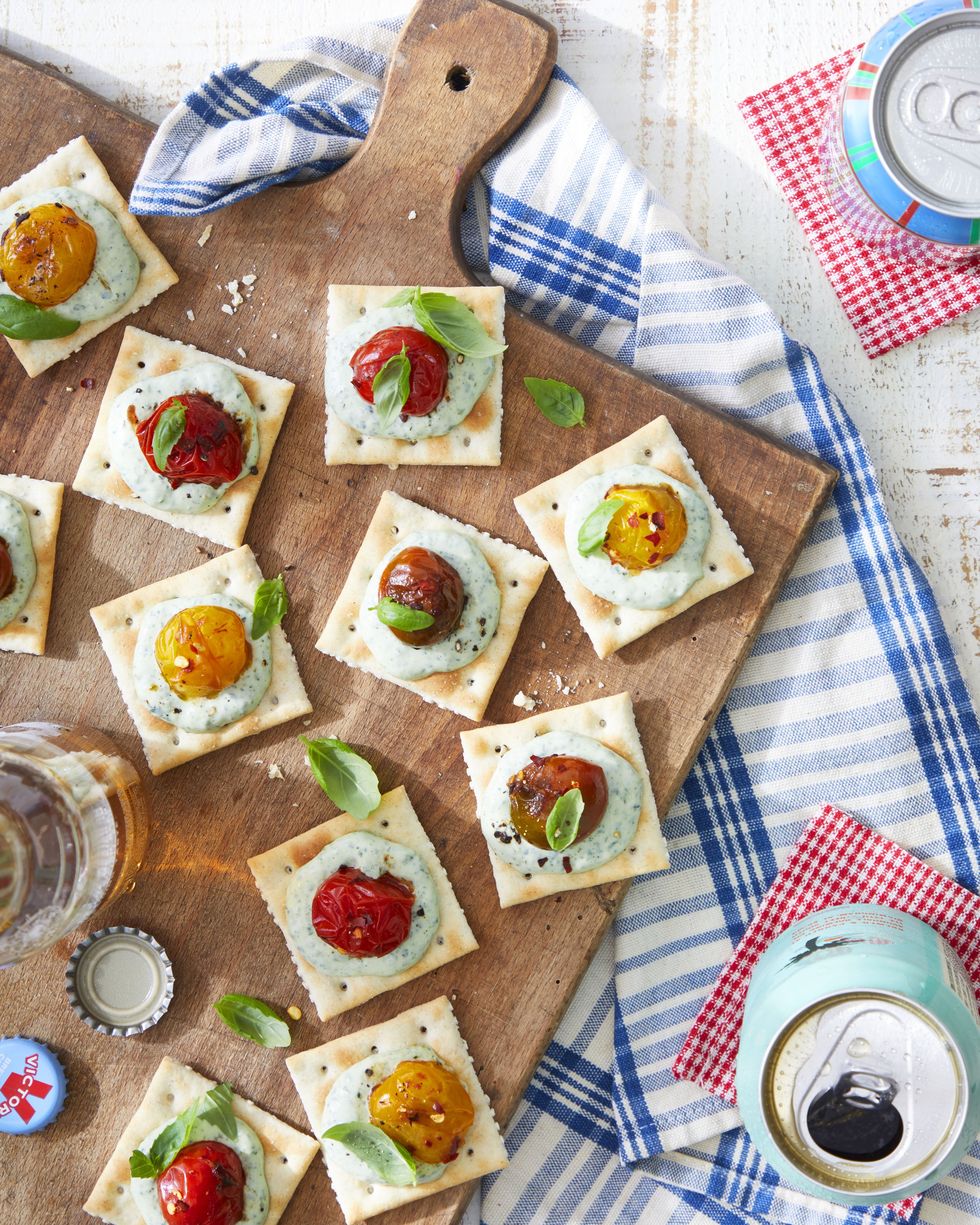 saltines with basil mayo and burst tomatoes on a wooden serving board and garnished with fresh basil