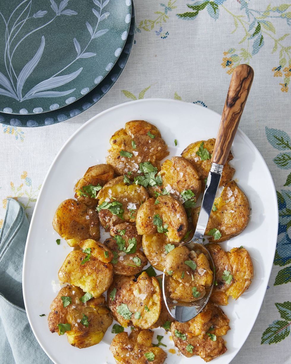 smashed potatoes with paprika and cumin on a white serving plate with a spoon for serving