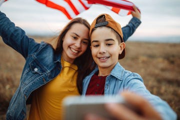 two young teens in field taking selfie with american flag that needs patriotic 4th of july caption