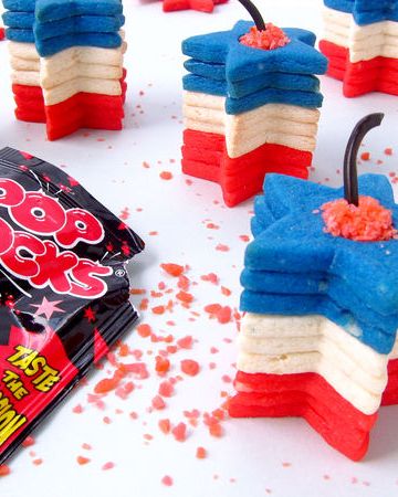 stack of red, white, and blue star shaped sugar cookies with licorice decoration on top to resemble fuse of a 4th of july firework