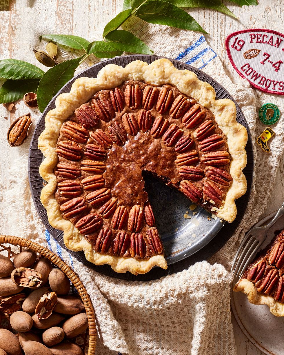 pecan brownie pie in a metal pie dish with a pice on a plate to the side and a bowl of unshelled pecans