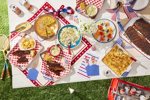 a table set with red white and blue for the fourth of july and filled with cornbread and ribs and slaw and fruit