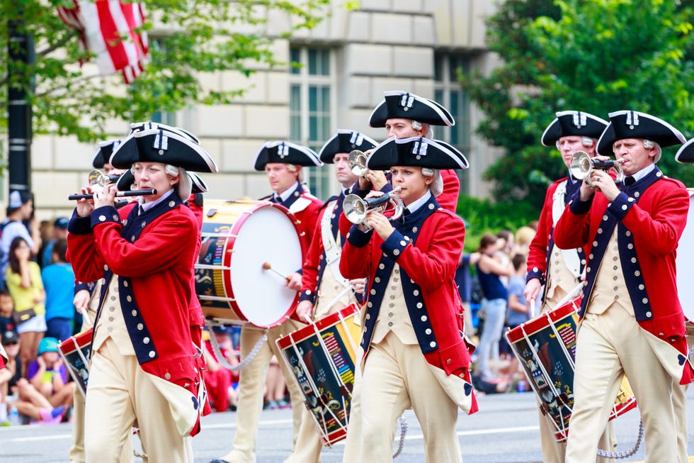 4th of july parade, parade members in uniforms with drums and a trumpet, good housekeeping's favorite 4th of july activities