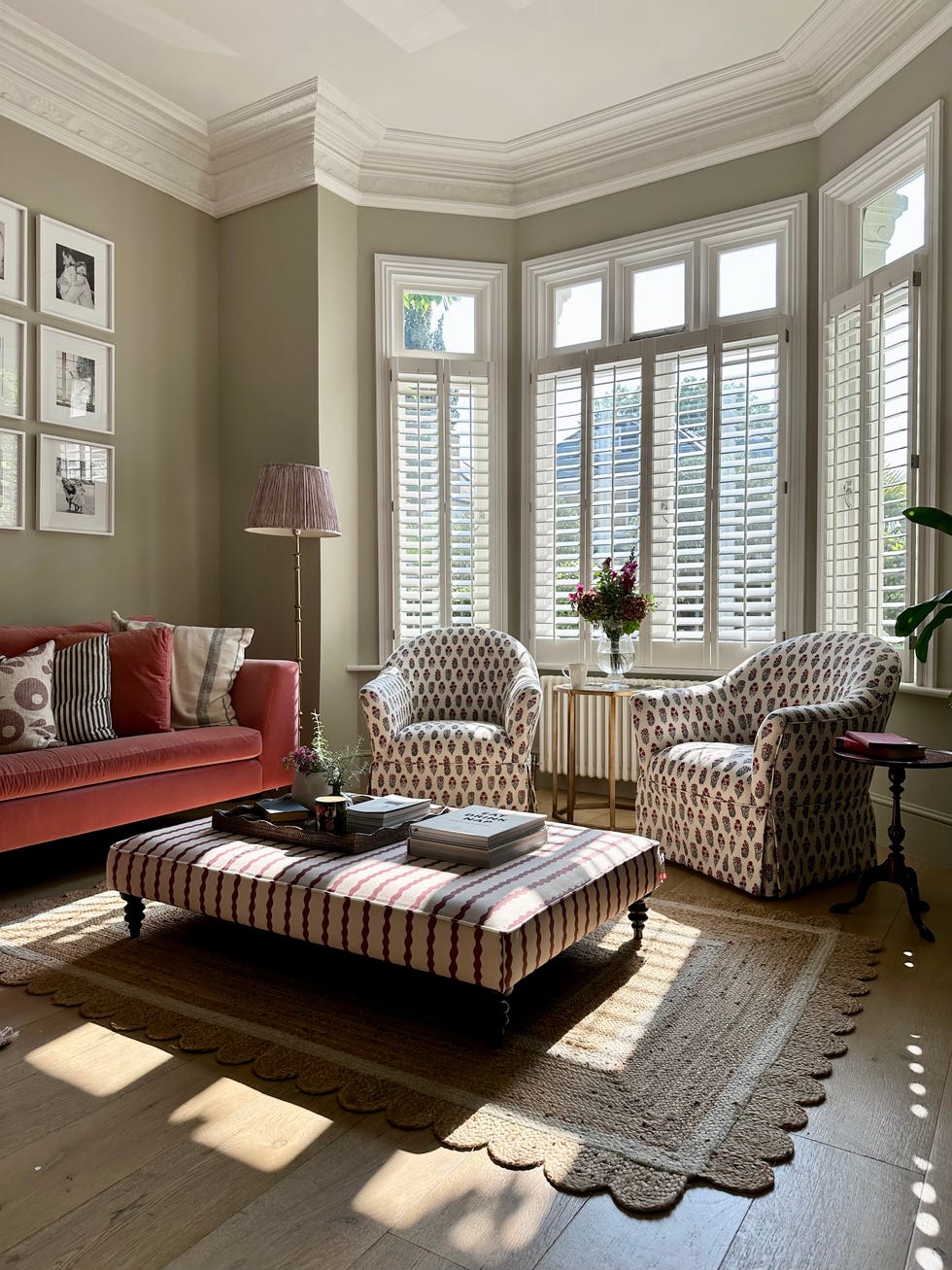 armchairs, sofa in a sage green living room with shutters