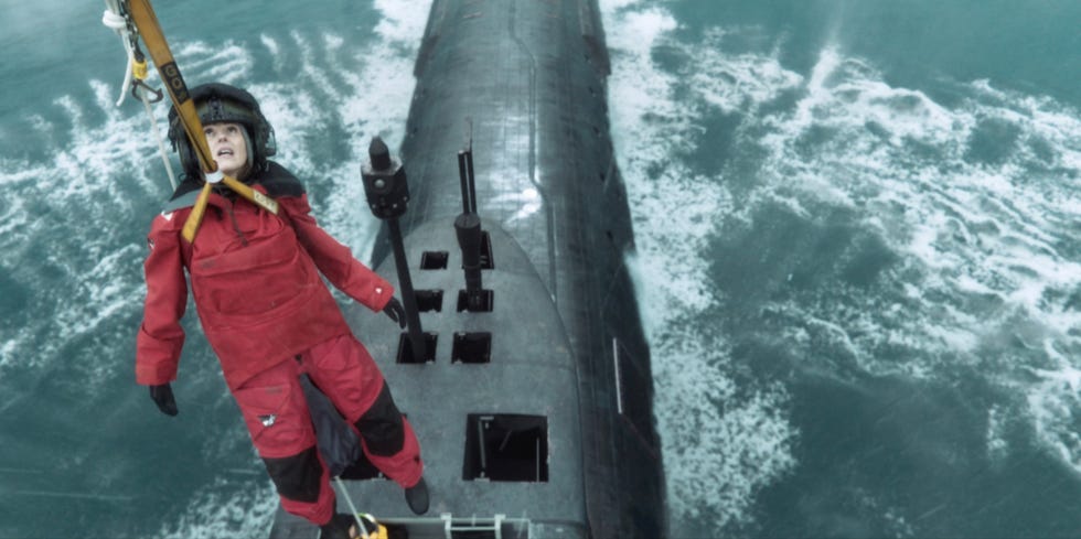 a person wearing a red waterproof suit is being hoisted above a submarine in the ocean