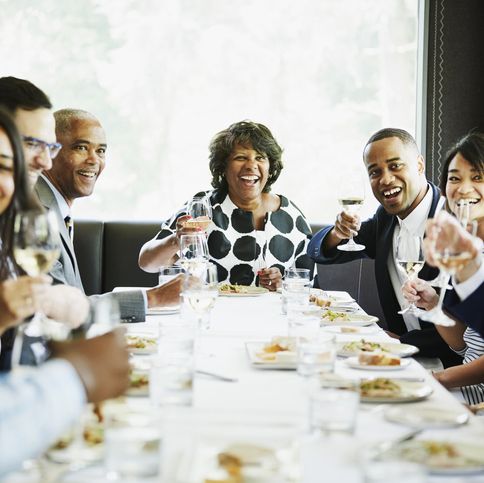 smiling and laughing group of family and friends preparing to toast during celebration meal in restaurant