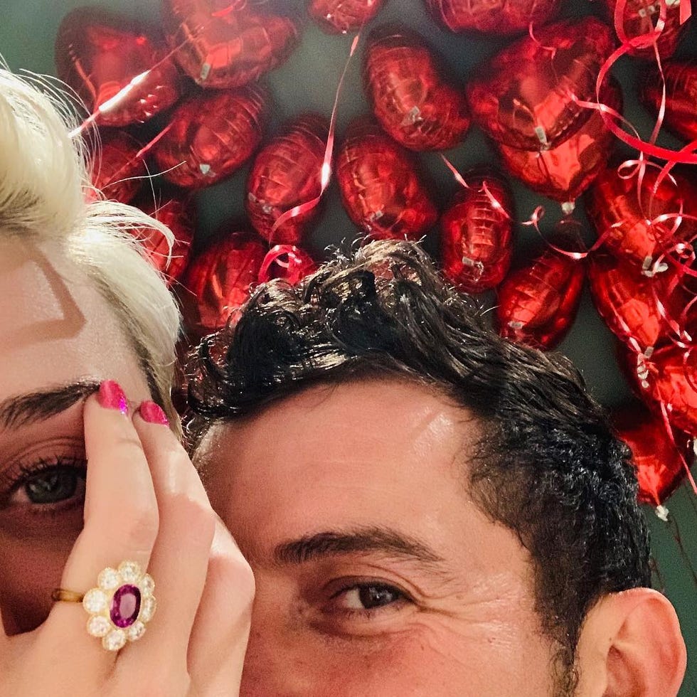 two people posing with red heartshaped balloons in the background