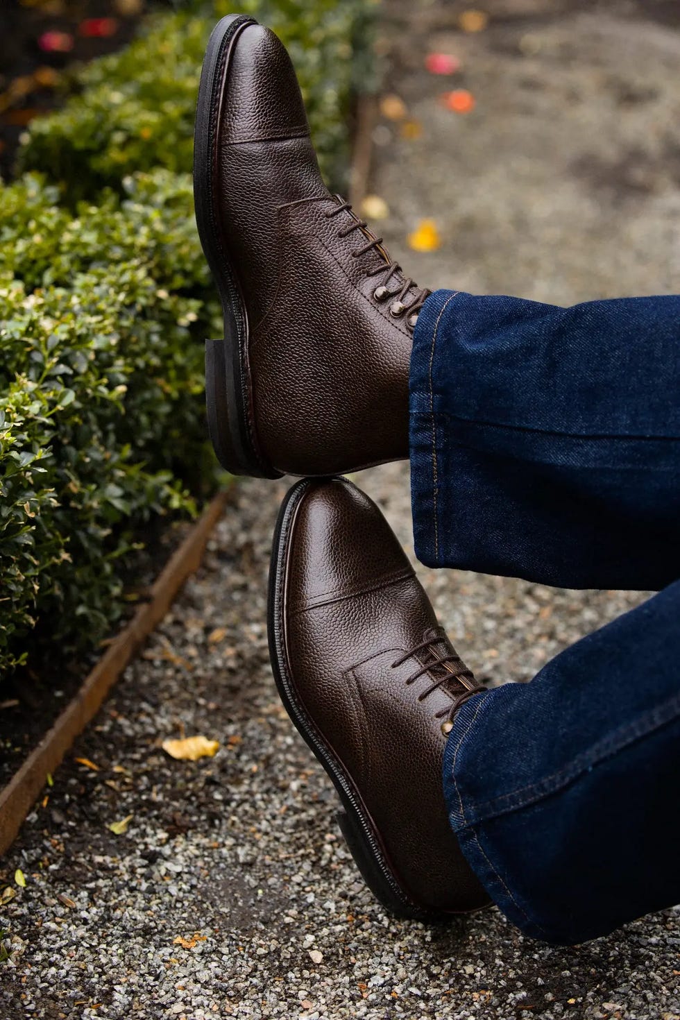 brown leather shoes resting near greenery and gravel