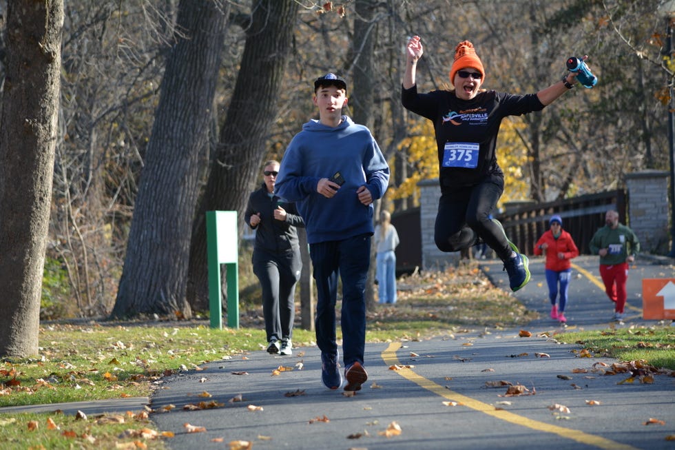participants running in a race along a paved path surrounded by trees and fallen leaves