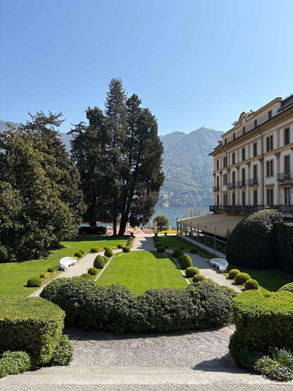 Historic villa surrounded by a manicured garden and mountains in the background.