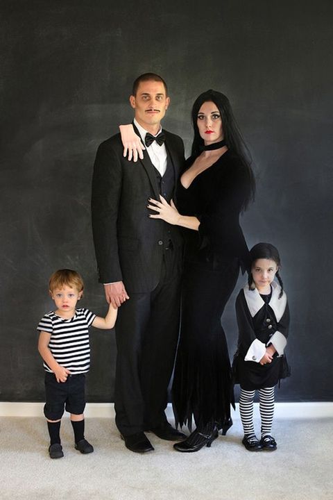 four people in a family halloween costume of the addams family, including gomez, morticia, wednesday and pugsley
