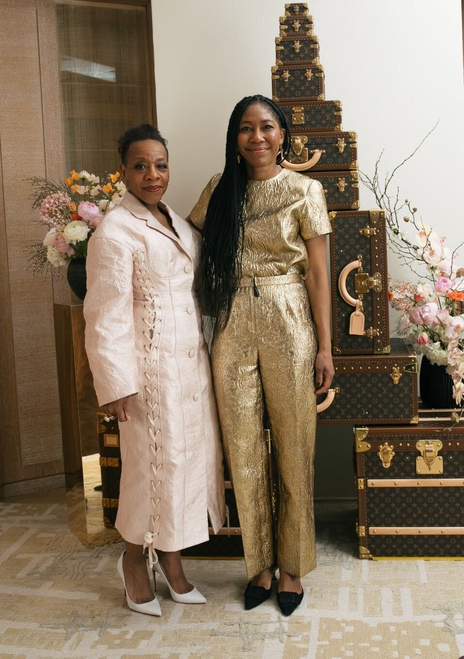 two women posing together with luxurious luggage and floral arrangements in the background