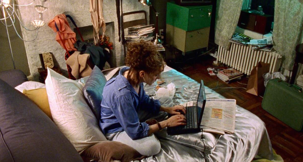 Individual working on a laptop in a cluttered bedroom.