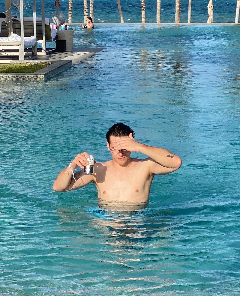 man in a pool holding a beer can and shielding his face from the sun