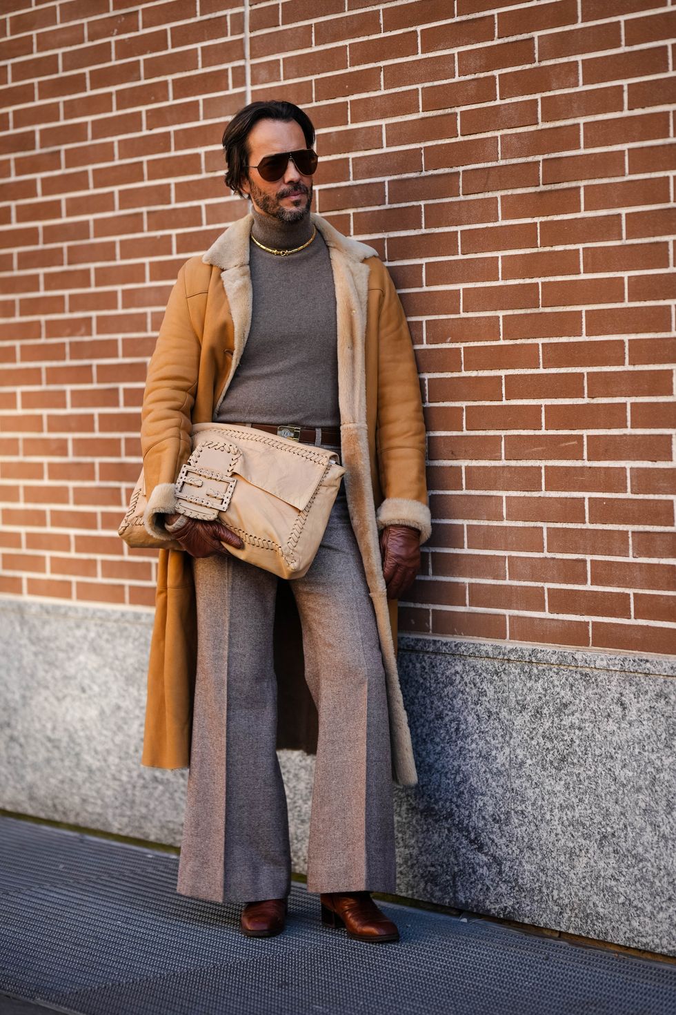 milan, italy january 13 a guest wears sunglasses, a golden necklace, a gray pullover, a leather belt, a large beige leather fendi bag, a brown leather long aviator coat, flared suit pants, brown pointed shoes, outside fendi, during the milan fashion week menswear fallwinter 2024 2025 on january 13, 2024 in milan, italy photo by edward berthelotgetty images