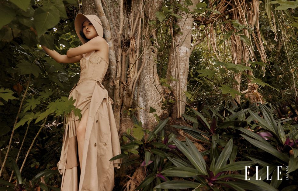 一個女人穿著連體衣風衣站在樹林裡