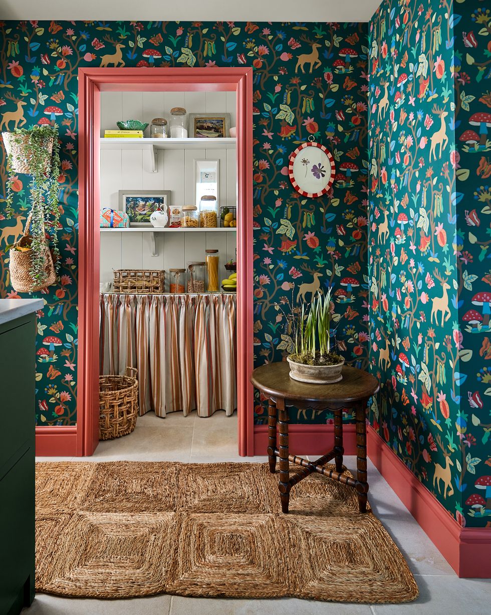 an open pantry for kitchen storage with botanical wallpaper and coral woodwork
