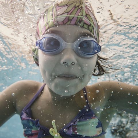 child with purple bathing suit swimming with goggles and swim cap