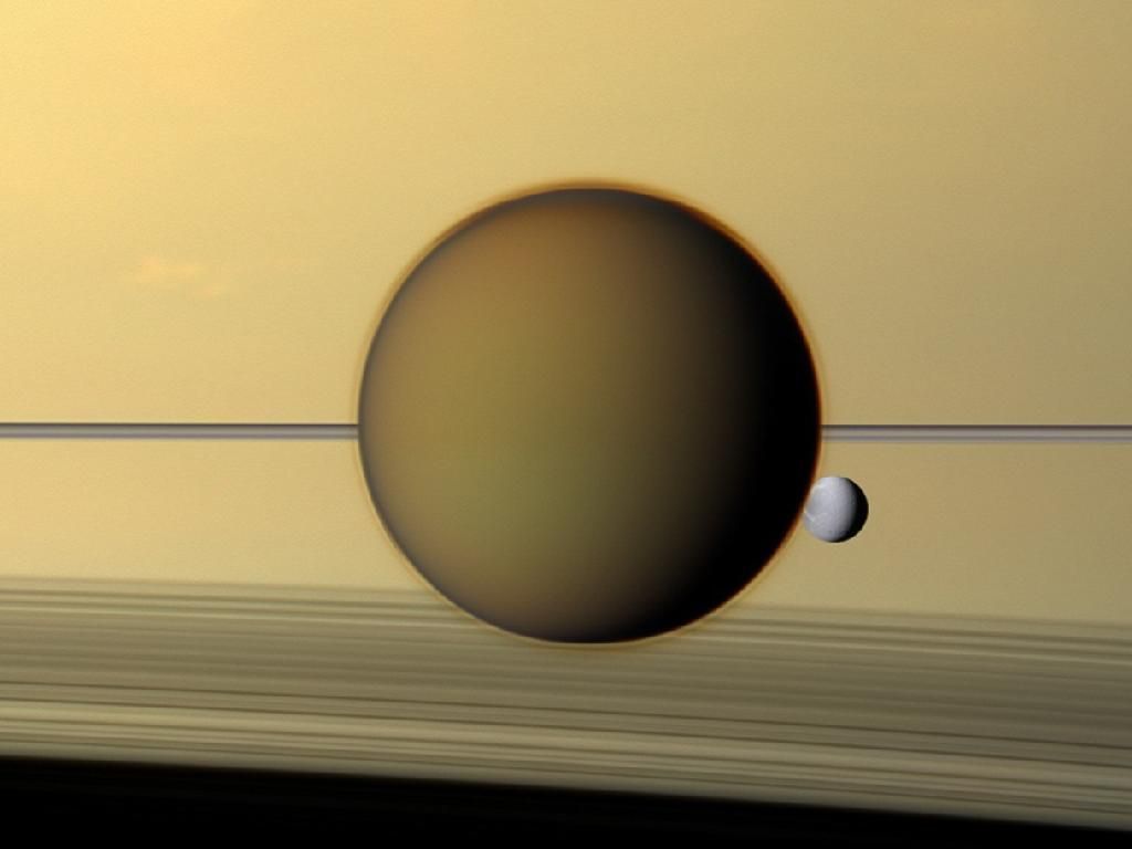 EEN NATUURLIJK KLEURENBEELD VAN SATURNUS WAZIGE EN ORANJE TITAN EN IJZIG WITTE DIONE DE RINGEN VAN SATURNUS ZIJN DE DUNNE LIJN DIE HET BEELD IN TWEEN DEELT