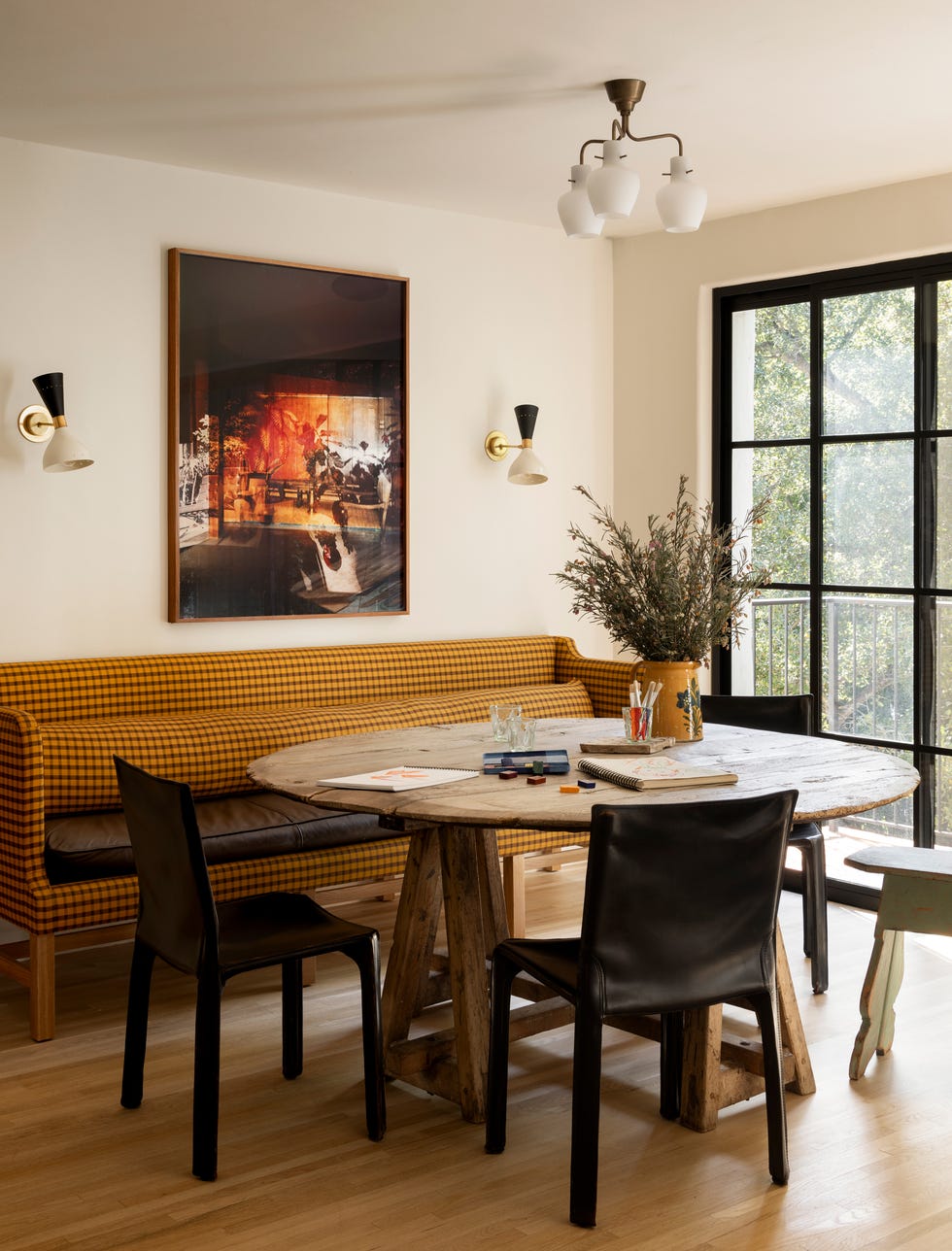 A dining area featuring a circular wooden table surrounded by black chairs and a yellow checked sofa.