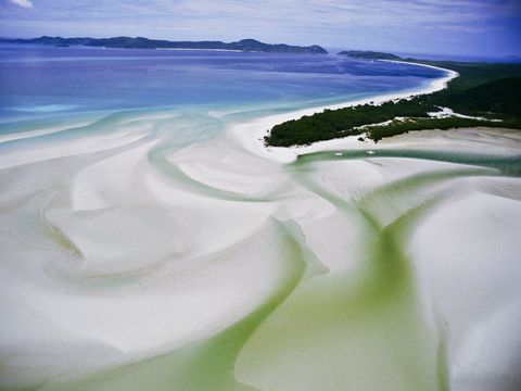 De vlakke zandkust van Australis Whitsundayeilanden en het natuurschoon van het omringende Groot Barrirerif trekken toeristen aan van over de hele wereld Veel van de 74 eilanden zijn aangewezen als nationaal park andere bieden onderdak aan luxueuze resorts