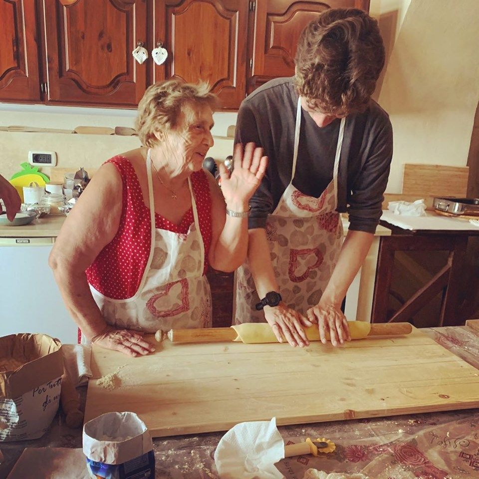 grandma teaching pasta making class with young man in italy