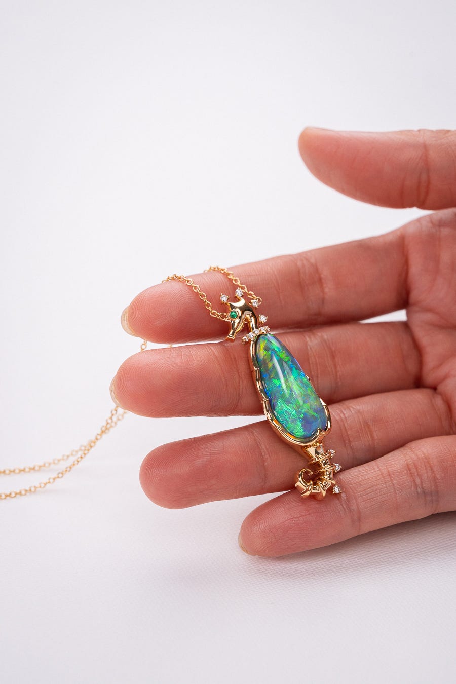 Hand holding a gold necklace with a large opal pendant.