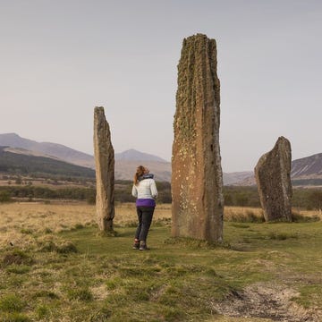 a person standing in a field with tall stone structures in the background
