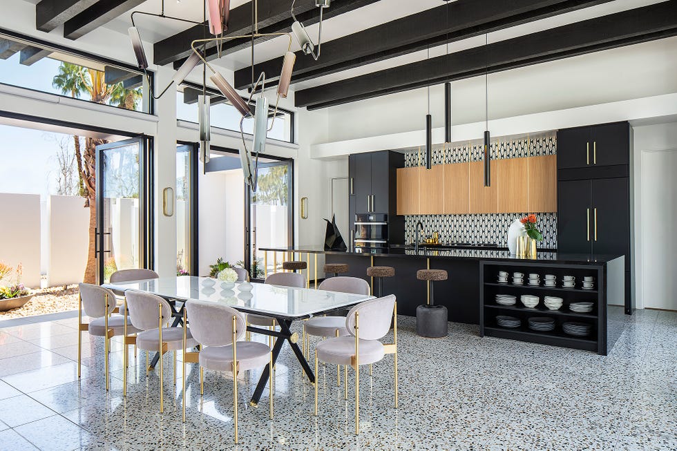 A dining room with a large black counter, white chairs and terrazzo floors