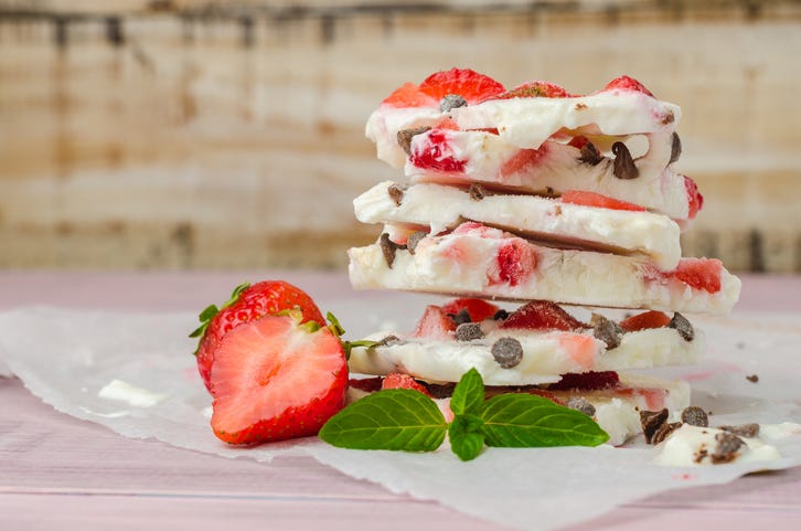 a stack of homemade healthy frozen yogurt bark with strawberries and chocolate chips on parchment paper, a healthy sweet snack