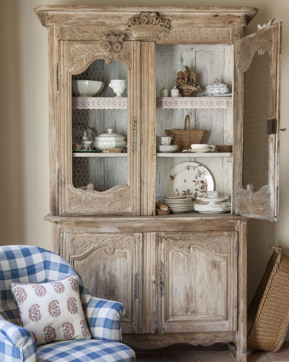 a rustic vintage kitchen dresser storing plates and crockery with a checked blue armchair in front