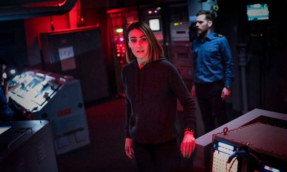 a scene set in a dimly lit control room with two individuals present