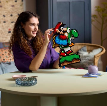 LEGO Super Mario and Yoshi set (LEGO 71428) a woman with long curly hair smiles as she sits in her living room at a round table building the super mario and yoshi lego display set