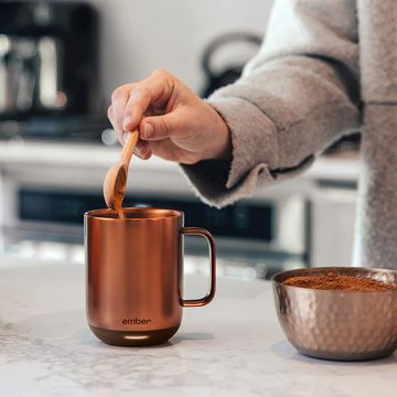 a hand adding instant coffee to a copper ember mug