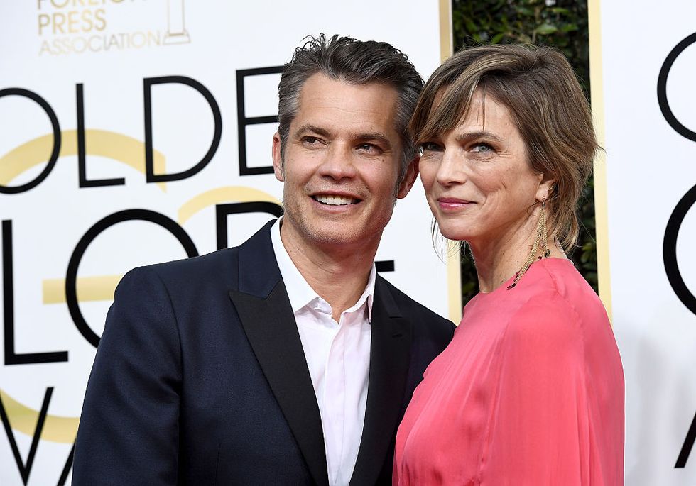 olyphant in navy suit and white button up, knief in red silk dress, pose on the red carpet at nbc's 74th golden globe awards