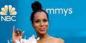 kerry washington in a white dress with floral appliques waving her right hand at the 74th primetime emmys arrivals in front of blue nbc emmys graphic