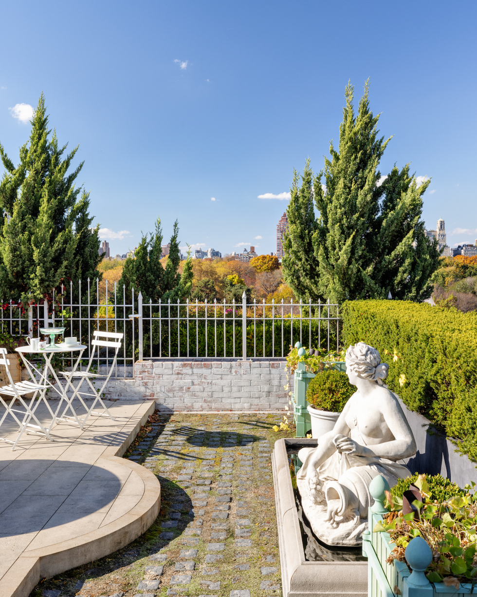 Rooftop patio featuring a statue and a seating area overlooking a skyline.