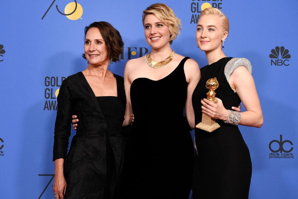 laurie metcalf, greta gerwig, and saoirse ronan wearing black dresses and smiling for a photo, as ronan holds a golden globe award