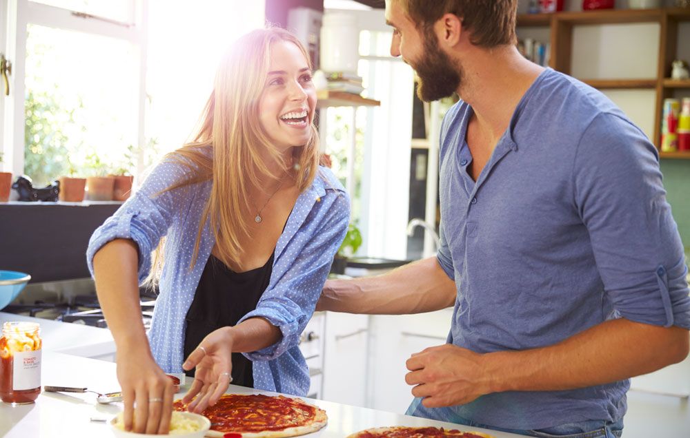A couple laughing and making pizza together. 