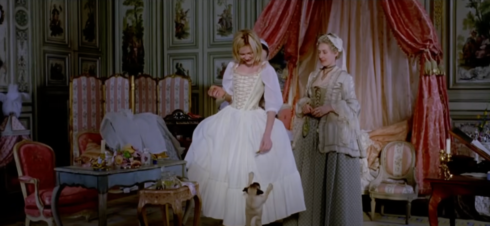 Scene depicting two women in historical costumes within a lavishly decorated room.