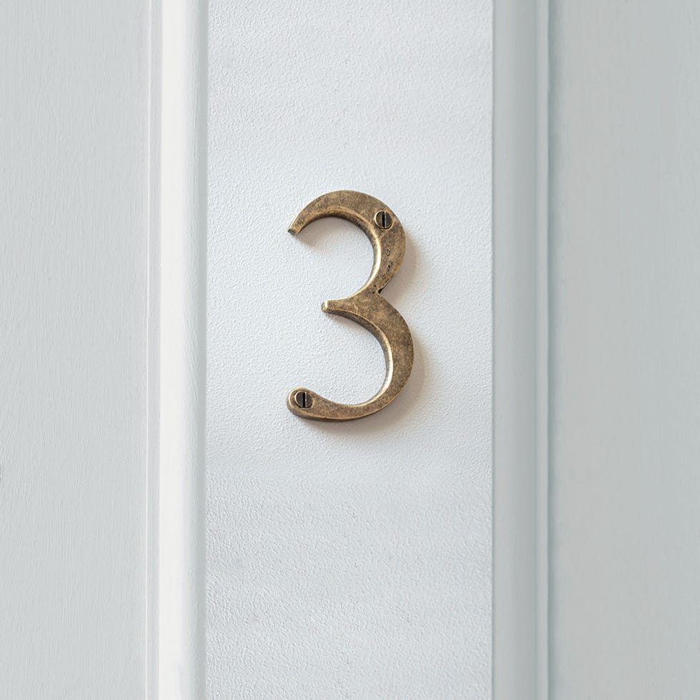 bronze house number 3 affixed to a white wall