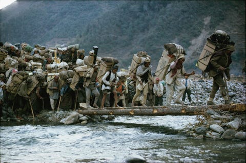 Op hun driehonderd kilometer lange tocht naar de Mount Everest steekt een groep van ruim negenhonderd dragers achter elkaar een brug van boomstammen over De dragers vervoerden 27 ton voorraden op hun rug bestemd voor de eerste Amerikaanse poging om de top van de Everest te beklimmen in 1963